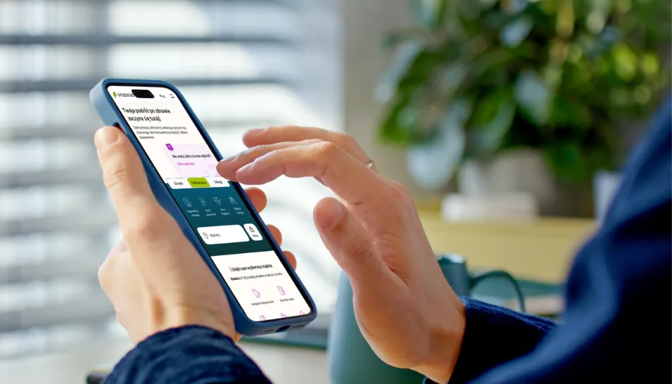 Dłoń seniora trzymająca smartfon z otwartym systemem rezerwacji obiektów zdrowotnych online, w tle rozmyte wnętrze salonu.